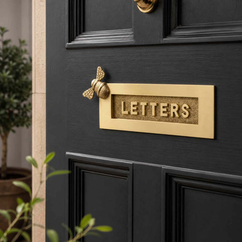 Satin brass bumble bee "LETTERS" letter plate fitted to a black front door, featuring a decorative bee motif and traditional raised lettering.