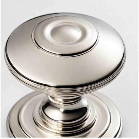 Macro close-up of a polished nickel round cupboard knob showing the raised centre and reeded detailing around the outer diameter.