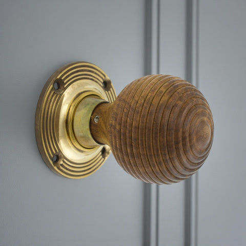 Rosewood beehive door knob with unlacquered aged brass backplate fitted to a grey door.