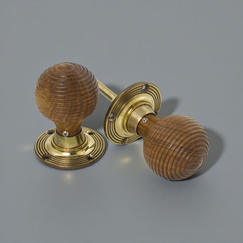 Pair of rosewood beehive door knobs with aged brass backplates displayed on a grey surface.
