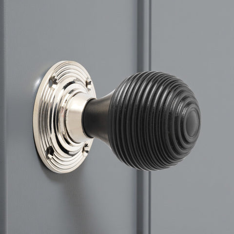 Close-up of an ebonised beehive door knob with polished nickel base mounted on a painted grey door.