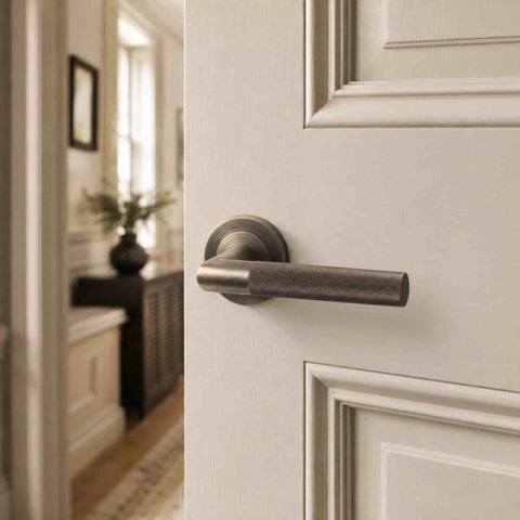 Antique brass knurled lever handle attached to a grey door with surroundings in the background.