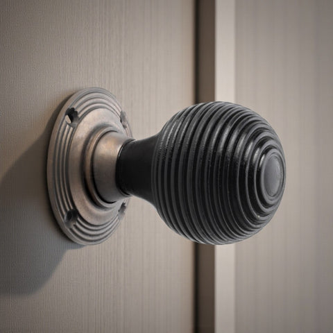 Side view of an ebonised beehive door knob on a matt antique backplate mounted to a wooden door.