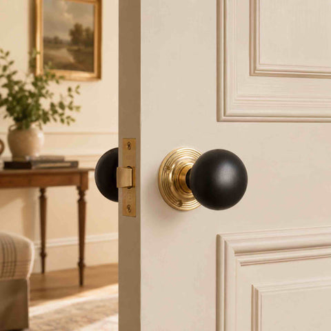 Ebonised black wood bun door knob pair with unlacquered polished brass backplates fitted to a cream panelled interior door.
