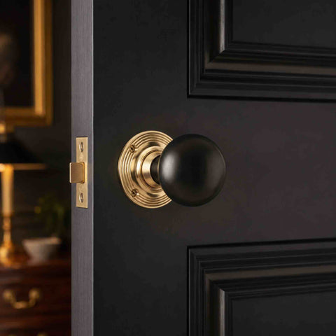 Ebonised black wood bun door knob with unlacquered polished brass backplate installed on a dark panelled interior door.