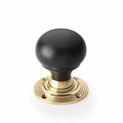 Single ebonised black wood bun rim mortice door knob with unlacquered polished brass reeded backplate on a white background.