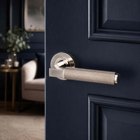 Polished nickel knurled lever handle on a navy blue panelled door with luxury interior background, highlighting the contemporary industrial style.
