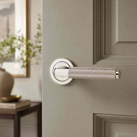 Polished nickel knurled internal door handle installed on a light grey door, demonstrating the clean modern finish and detailed knurled texture.
