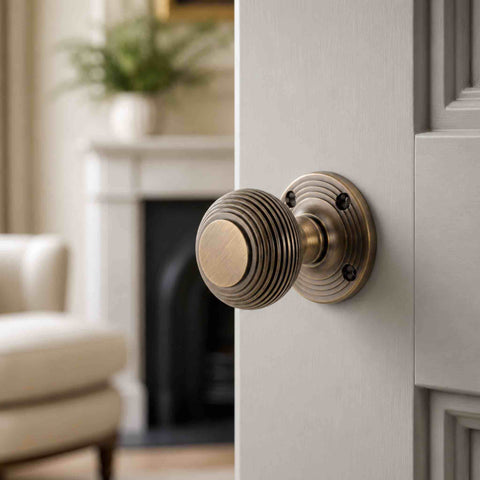 Matt antique brass sprung beehive mortice door knob fitted to a grey painted interior door in a traditional living room setting.