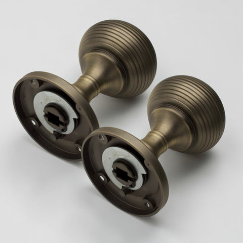 Pair of matt antique brass sprung beehive mortice door knobs showing the concealed sprung mechanism and fixing backplates.