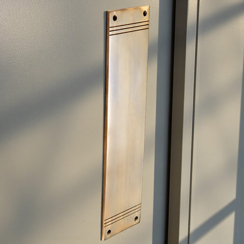 Unlacquered aged brass reeded push plate fitted to painted door, showing vertical installation and natural patina