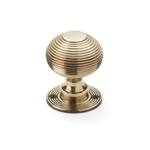 Single aged brass reeded beehive mortice door knob with circular reeded rose on white background