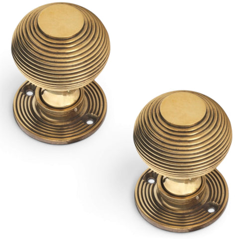 Pair of aged brass reeded beehive door knobs shown from angled top view with decorative reeded backplates