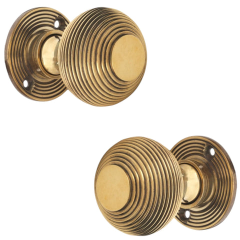 Pair of aged brass reeded beehive mortice door knobs shown from side profile angle on white background