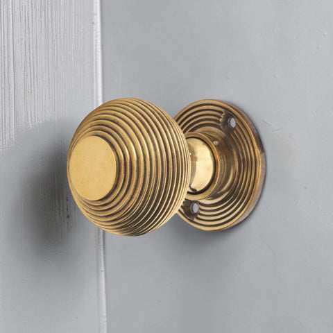 Aged brass reeded beehive mortice door knob installed on painted grey wooden door