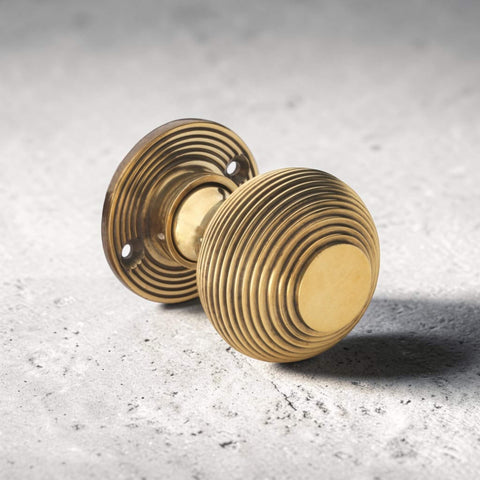 Single aged brass reeded beehive mortice door knob resting on textured surface with decorative reeded rose