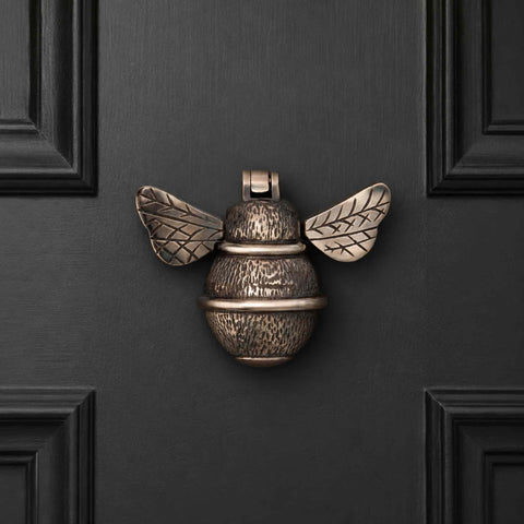 Aged brass bumble bee door knocker mounted on a black panelled entrance door