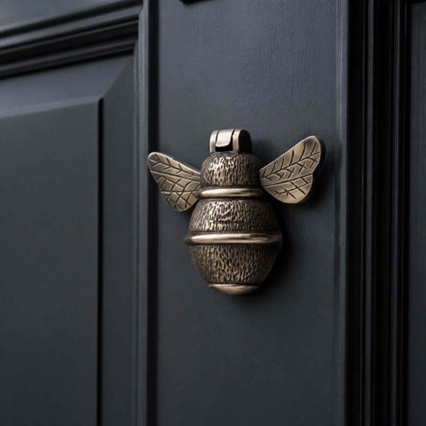 Aged brass bumble bee door knocker fitted to a black front door showing traditional styling