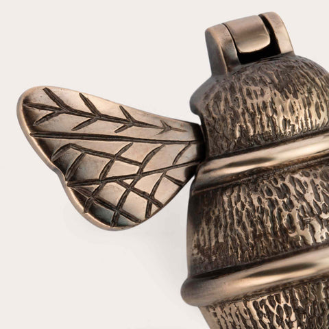 Close-up of aged brass bumble bee door knocker highlighting engraved wing detailing
