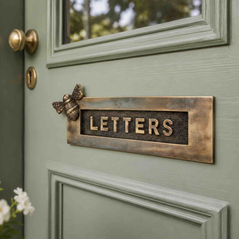 Close angled view of the aged brass bumble bee letter plate highlighting the textured centre and decorative bee detail.