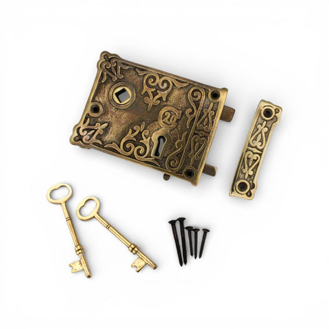 Aged brass floral rim lock set including lock body, keep, two brass keys, and fixing screws on a white background.