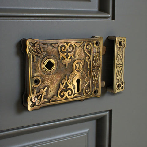 Aged brass floral rim lock fitted to a traditional panel door with matching decorative keep.