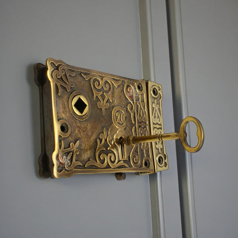 Aged brass floral rim lock fitted to a painted door with key inserted, showing ornate decorative detailing.