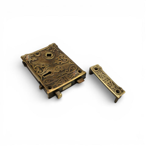 Unlacquered aged brass floral rim lock with matching keep displayed on a white background.