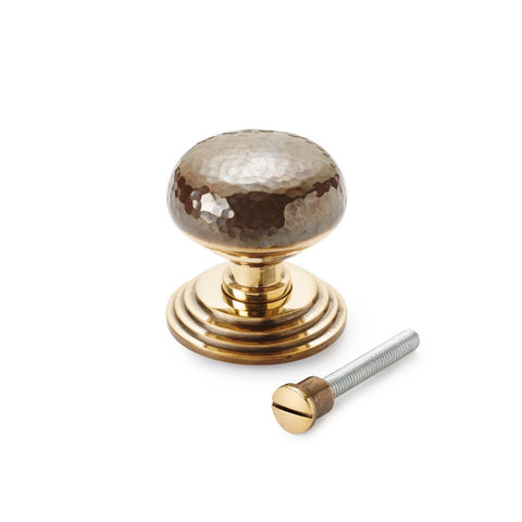 Unlacquered aged brass hammered centre door knob supplied with fixing bolt on white background