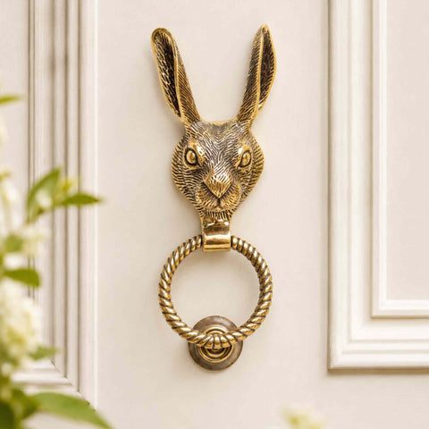 Aged brass hare door knocker with reeded ring mounted on a cream panelled front door.