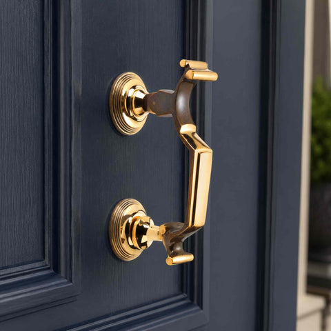 Side profile of an Aged Brass Reeded Doctor Door Knocker fitted to a dark blue front door, highlighting the solid brass construction, reeded detailing and premium aged brass finish.