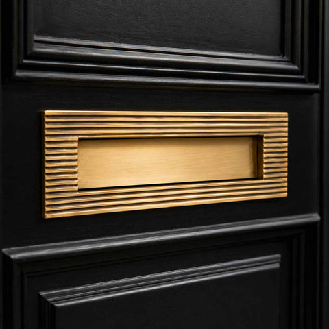 Close-up of reeded solid brass letter plate with unlacquered aged brass finish on a traditional black door