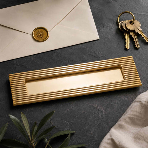 Reeded solid brass letter box plate in aged brass finish displayed with keys and envelope