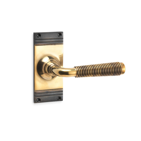 Aged brass reeded lever on rectangular backplate, solid brass door handle photographed on a white background.