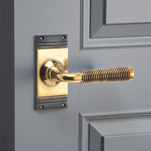 Aged brass reeded lever door handle on backplate fitted to grey panelled door