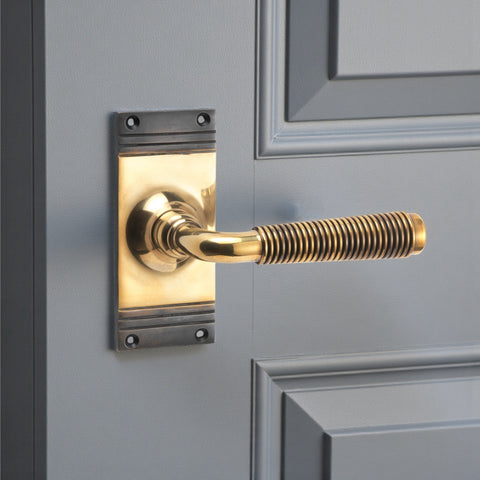 Aged brass reeded lever on backplate fitted to a painted panel door, showing warm unlacquered finish.