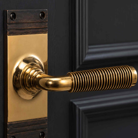 Close-up of aged brass reeded lever door handle showing detailed reeded grip and backplate finish