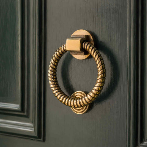 Aged brass reeded ring door knocker installed on a traditional dark front door