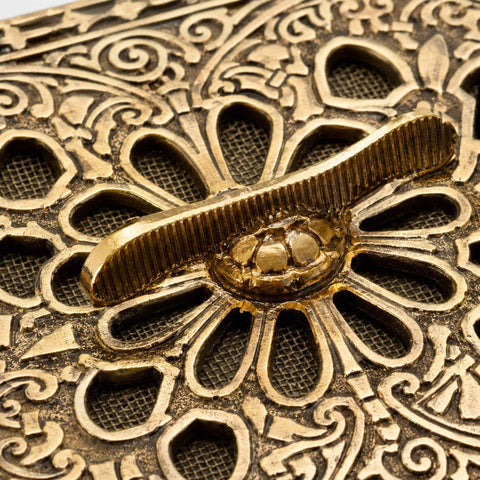Macro close-up of the aged brass air vent slider mechanism, highlighting the detailed casting, antique finish and intricate floral pattern.