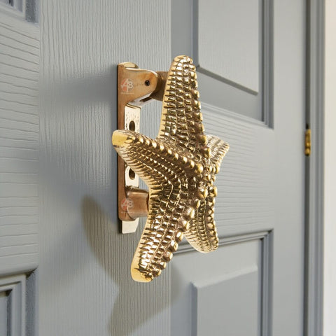 Unlacquered aged brass starfish door knocker fitted to painted front door, showing coastal decorative design