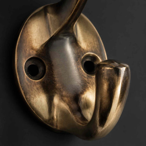 Close-up of an unlacquered aged brass Victorian coat hook showing the round fixing plate and lower hook