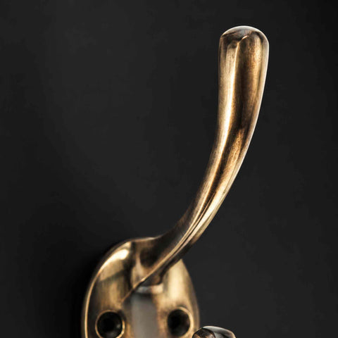 Close-up side view of a solid brass Victorian coat hook showing the curved upper hook and aged finish