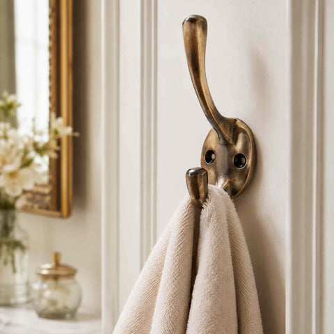 Aged brass Victorian double coat hook mounted on a traditional panelled wall holding white towels