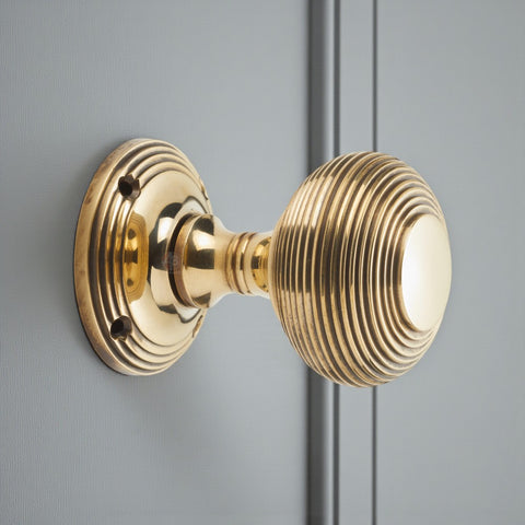 Side view of aged brass beehive door knob installed on a door, highlighting the reeded design and round backplate.