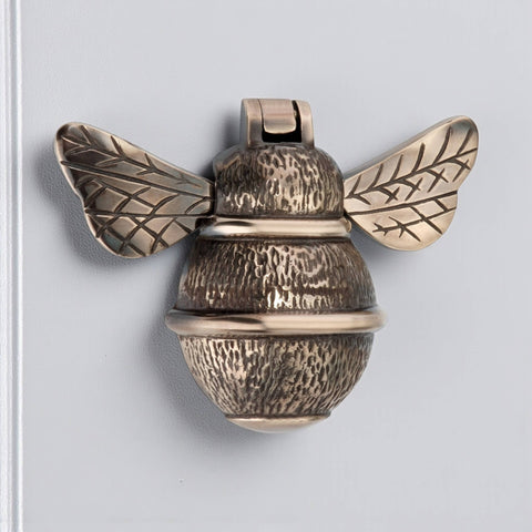 Unlacquered aged brass bumble bee door knocker front view showing detailed wings and textured body on door