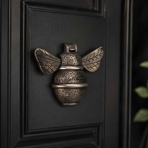 Aged brass bumble bee door knocker mounted on a black panelled entrance door