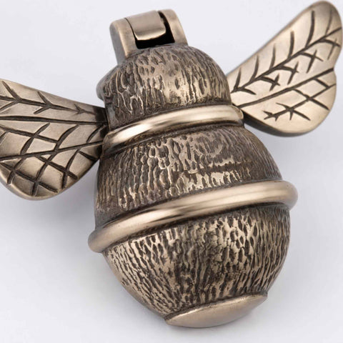 Close-up of aged brass bumble bee door knocker showing decorative wing engraving and antique finish