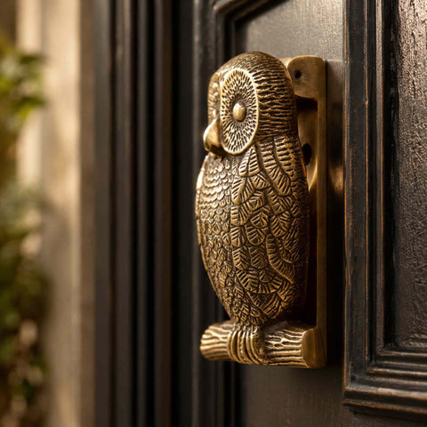 Side profile of the aged solid brass owl door knocker fitted to a black entrance door, displaying the depth, craftsmanship and antique finish.