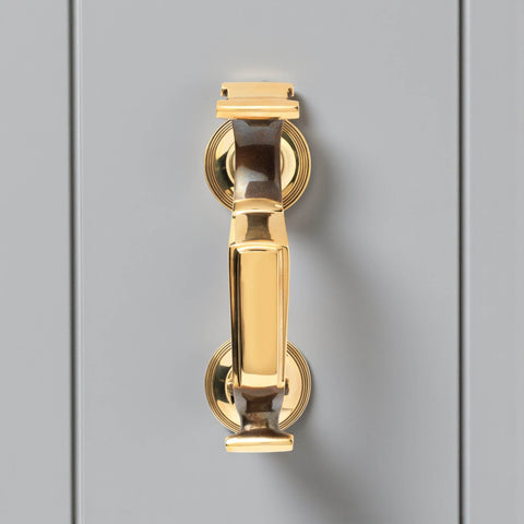 Front view of unlacquered aged brass reeded doctor door knocker on grey door, displaying traditional doctor style design and polished brass finish.