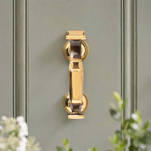 Aged Brass Reeded Doctor Door Knocker displayed on a sage green front door, highlighting the warm brass finish and traditional styling.